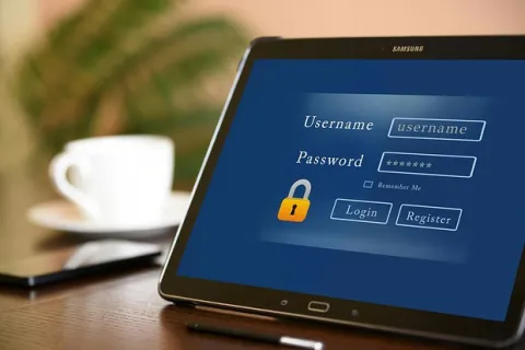 Tablet displaying login screen with username and password fields on wooden table with coffee cup and phone nearby