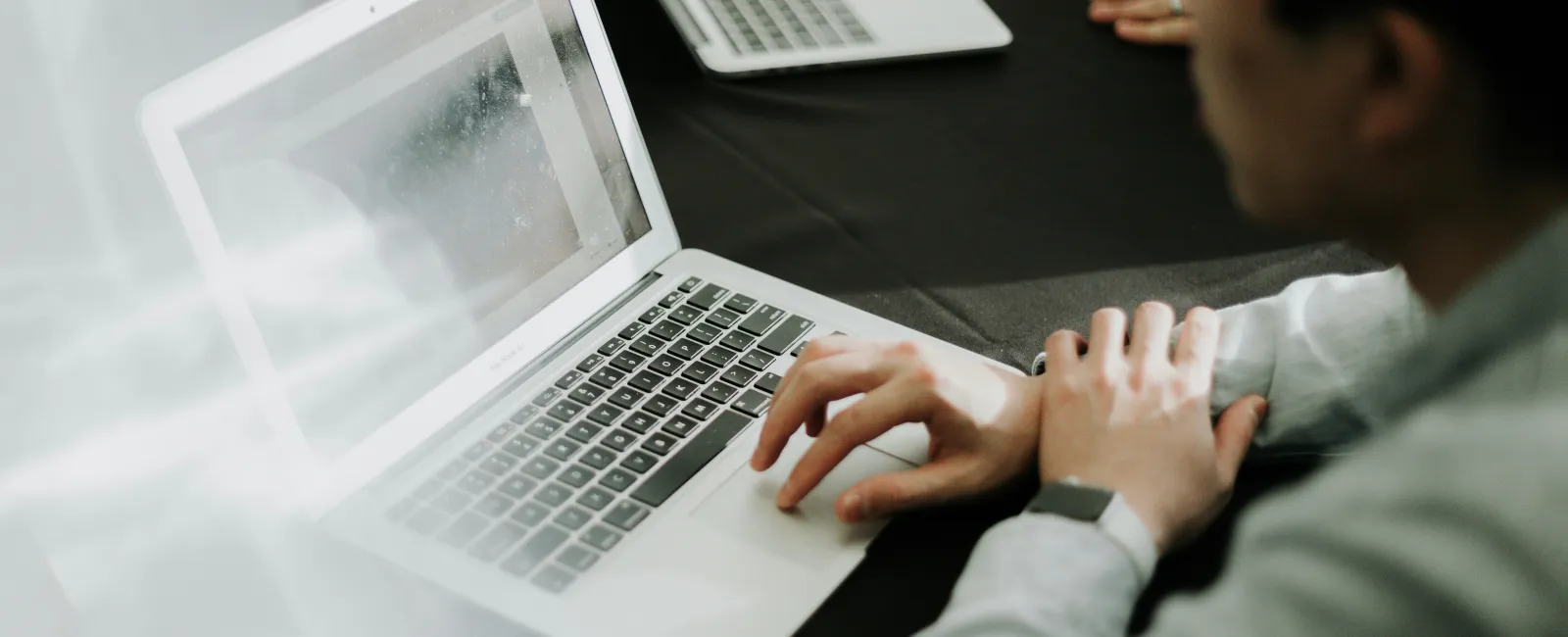 Person working on a laptop with another laptop visible on a black table in a collaborative workspace.