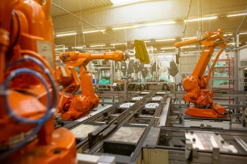 Orange robotic arms operating on an automated production line inside a modern manufacturing facility.