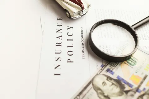 Magnifying glass, toy car, and US dollar bill on an insurance policy document.