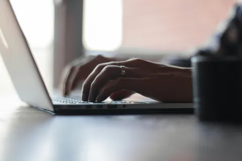 Close-up of hands typing on a laptop keyboard in soft natural light with blurred background