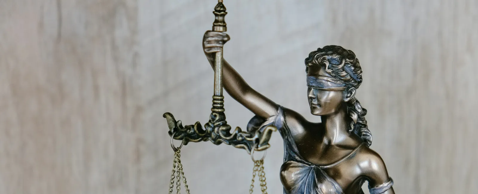 Bronze statue of Lady Justice blindfolded holding balanced scales against a neutral background