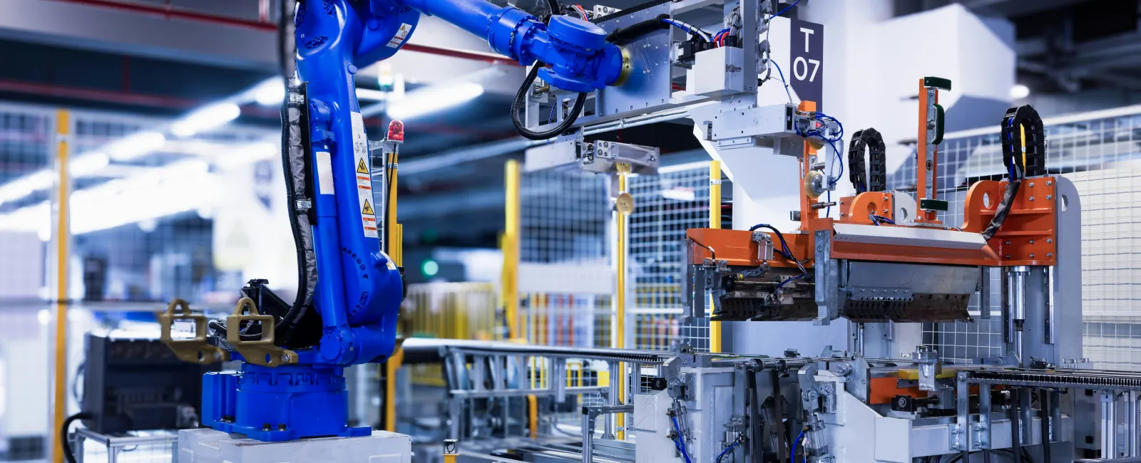 Blue industrial robotic arm operating automated machinery in a modern factory setting with metallic and orange components.