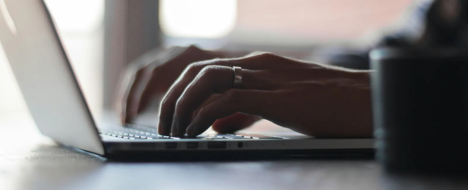 Close-up of hands typing on a laptop keyboard with natural light and blurred background.