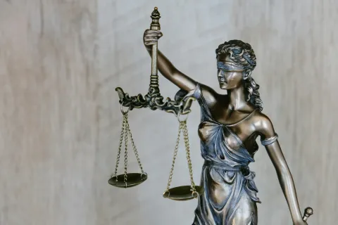 Bronze statue of Lady Justice blindfolded holding scales symbolizing fairness and law against a wooden background
